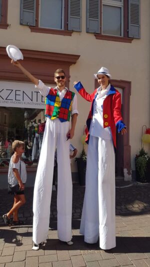 Stelzenläufer winken auf einem Strassenfest den Passanten zu